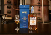 A bottle of Mount Gay The Coffey Still Expression rum sits next to its blue packaging with a sniffing glass with the rum inside.