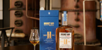 A bottle of Mount Gay The Coffey Still Expression rum sits next to its blue packaging with a sniffing glass with the rum inside.