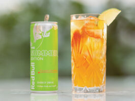 Energising soft drinks with Red Bull A can of Red Bull Curuba Summer Edition is next to a glass filled with the energy drink on a table with greenery blurred in the background.