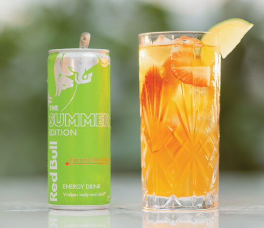 Energising soft drinks with Red Bull A can of Red Bull Curuba Summer Edition is next to a glass filled with the energy drink on a table with greenery blurred in the background.