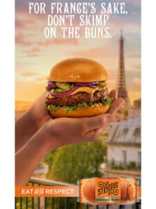Someone holds a burger up against the Paris skyline with the Eiffel Tower in the background. Text reads For France's sake, don't skimp on the buns.