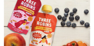 Two packs of the new Three Robins oat milk Smoothie pouches sit on a table with fruit and vegetables around them.