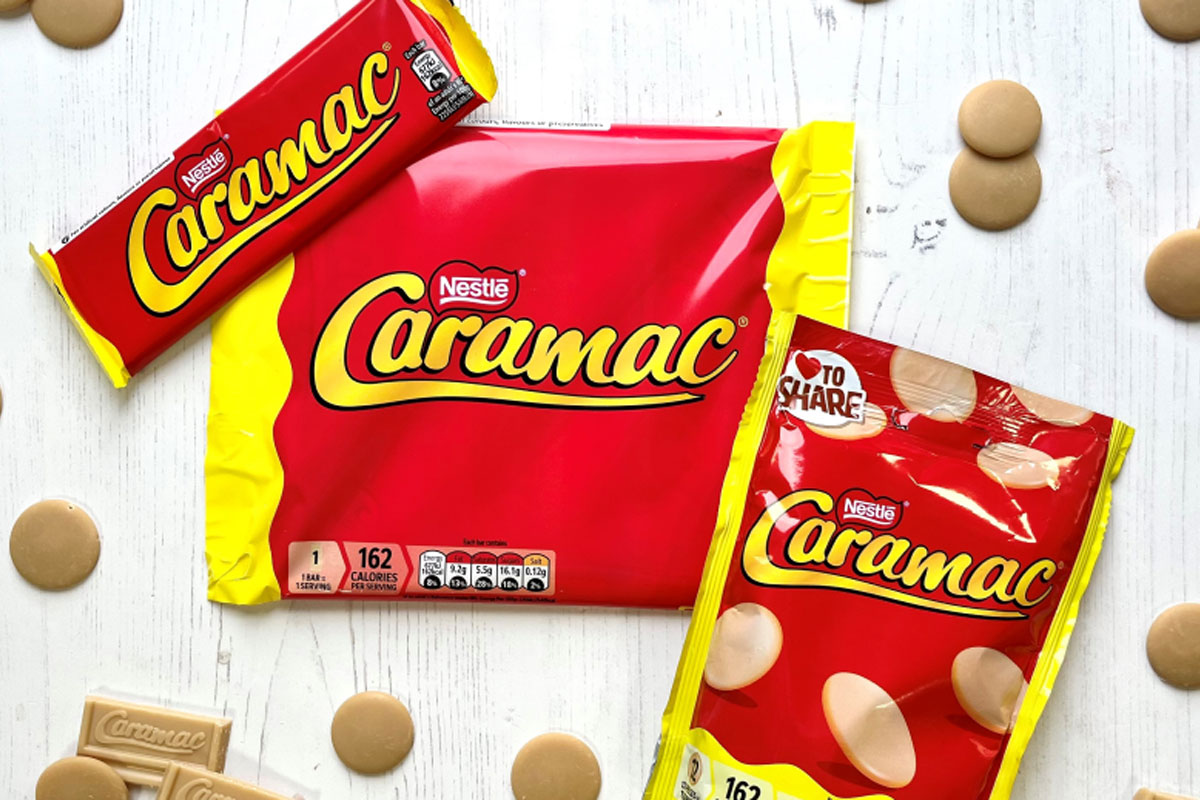 Packs of Caramac including a bar, multipack of bars and sharing pack, sit on a white wooden background with pieces of the blonde chocolate around them.
