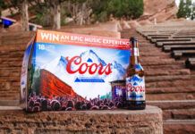 A pack of Coors lager sits on a rock step with a bottle of Coors lager to its side with red rock steps in the background.