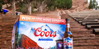 A pack of Coors lager sits on a rock step with a bottle of Coors lager to its side with red rock steps in the background.