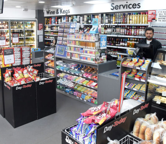 Inflation trickles down on consumer goods A Day-Today store floor with the counter area, product bins close to the checkout and a staff member behind the till.