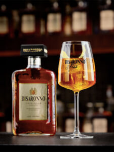 A bottle of Disaronno Originale stands next to a Disaronno Fizz cocktail serve in a bar.