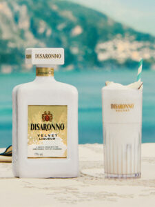 A bottle of Disaronno Velvet stands next to a cocktail serve made using the drink with a holiday scene in the background.