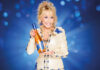 Dolly Parton holds a bottle of Dolly Wine Rose against a blue background.