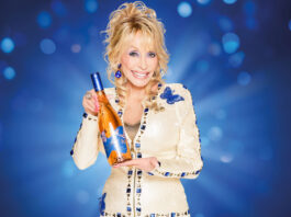 It’s Wine to Five as Dolly Parton launches new wines in UK Dolly Parton holds a bottle of Dolly Wine Rose against a blue background.
