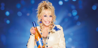 Dolly Parton holds a bottle of Dolly Wine Rose against a blue background.