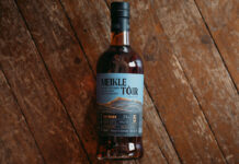 A bottle of GlenAllachie Meikle Tòir Turbo 2024 Edition rests against a wooden floor.