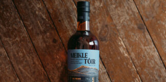 A bottle of GlenAllachie Meikle Tòir Turbo 2024 Edition rests against a wooden floor.