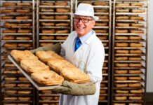 Gordon Allan holds a tray of steak pies with trays stacked up behind him.