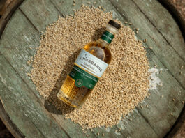 A bottle of Kingsbarns Coaltown lies on top of a pile of grain on top of a wooden barrel.