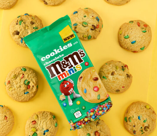 Add in colour with new M&M’s Minis Cookies A pack of M&M's Minis Cookies sit on top of a yellow background with the cookies around the pack.