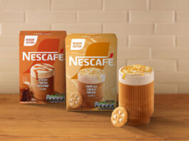 Nescafé indulges a sweet tooth in new coffee Boxes of Nescafé Dessert Edition Vanilla Cookie Dough and Sticky Toffee Pudding coffee sit on a countertop with a white tile wall behind them and a glass of coffee with a cookie next to the packs.