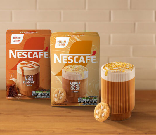 Nescafé indulges a sweet tooth in new coffee Boxes of Nescafé Dessert Edition Vanilla Cookie Dough and Sticky Toffee Pudding coffee sit on a countertop with a white tile wall behind them and a glass of coffee with a cookie next to the packs.