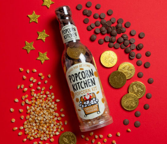 Popcorn Kitchen pops in the home for Christmas A pack shot of Popcorn Kitchen Chocolate Treasure sits against a red background with popcorn kernels and chocolate pieces and coins around it.