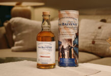 A bottle of The Balvenie A Collection of Curious Casks 14 Year Old American Bourbon Barrel stands next to its case on top of a white couch.