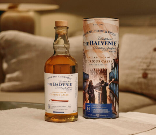 Open up to Curiosity with new whisky from The Balvenie A bottle of The Balvenie A Collection of Curious Casks 14 Year Old American Bourbon Barrel stands next to its case on top of a white couch.