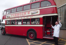 Sir Boyd Tunnock stands next to a vintage double decker bus with a Tunnock's Caramel Wafer advert on its side.