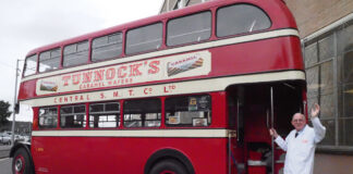 Sir Boyd Tunnock stands next to a vintage double decker bus with a Tunnock's Caramel Wafer advert on its side.