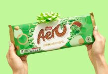 A person holds an Aero Peppermint Sharing Bar against a green background with a green bow on top of the bar.