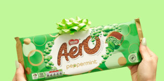 A person holds an Aero Peppermint Sharing Bar against a green background with a green bow on top of the bar.