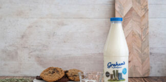 A bottle of Graham's whole milk stands next to a plate with chocolate chip cookies on it.