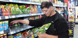 A man is stocking shelves with crisps in a convenience store.