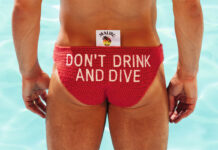 Olympic diver Tom Daley stands in front of a pool in diving clothing with a Malibu branded tag sticking out the clothes with the text reading 'Don't Drink and Dive'.