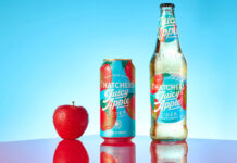 A bottle of Thatchers Juicy Cider Juicy Apple is next to a can of Thatchers Cider Juicy Apple with a red apple next to the can against a blue background with a shiny red table underneath.