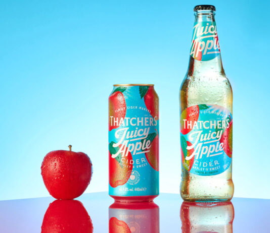 Thatchers Cider rolls a Juicy launch to retail A bottle of Thatchers Juicy Cider Juicy Apple is next to a can of Thatchers Cider Juicy Apple with a red apple next to the can against a blue background with a shiny red table underneath.