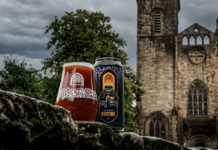 A can of Vault City Black Grape Buckie V.2 stands next to a glass filled with the sour beer in front of the ruins of a church building.