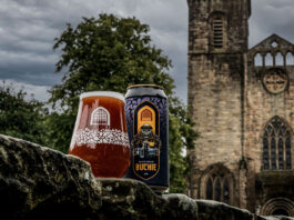 Buckie-inspired beer returns from the Vault A can of Vault City Black Grape Buckie V.2 stands next to a glass filled with the sour beer in front of the ruins of a church building.