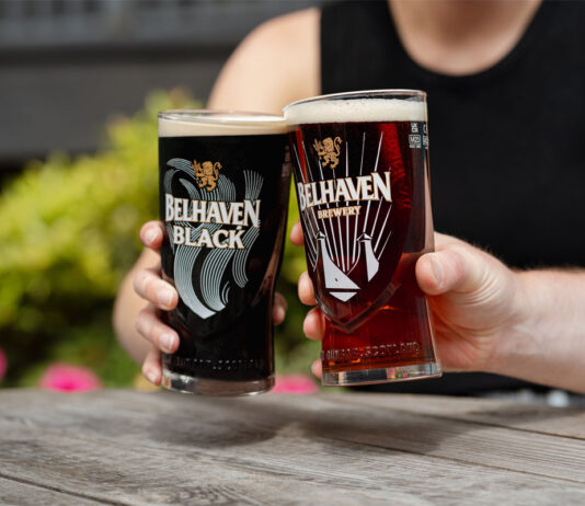 Belhaven serves a double win Two people sit holding Belhaven branded glasses with beer inside them and clink them together.