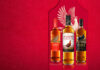 Bottles of The Famous Grouse range lined up against a red background with the illustration of a grouse behind the bottles.