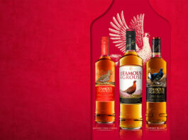 The Famous Grouse moves to William Grant & Sons Bottles of The Famous Grouse range lined up against a red background with the illustration of a grouse behind the bottles.