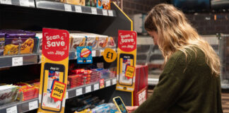 A woman uses her phone to redeem rewards of Jisp's Scan & Save app with promotions highlighting the app on store shelves.