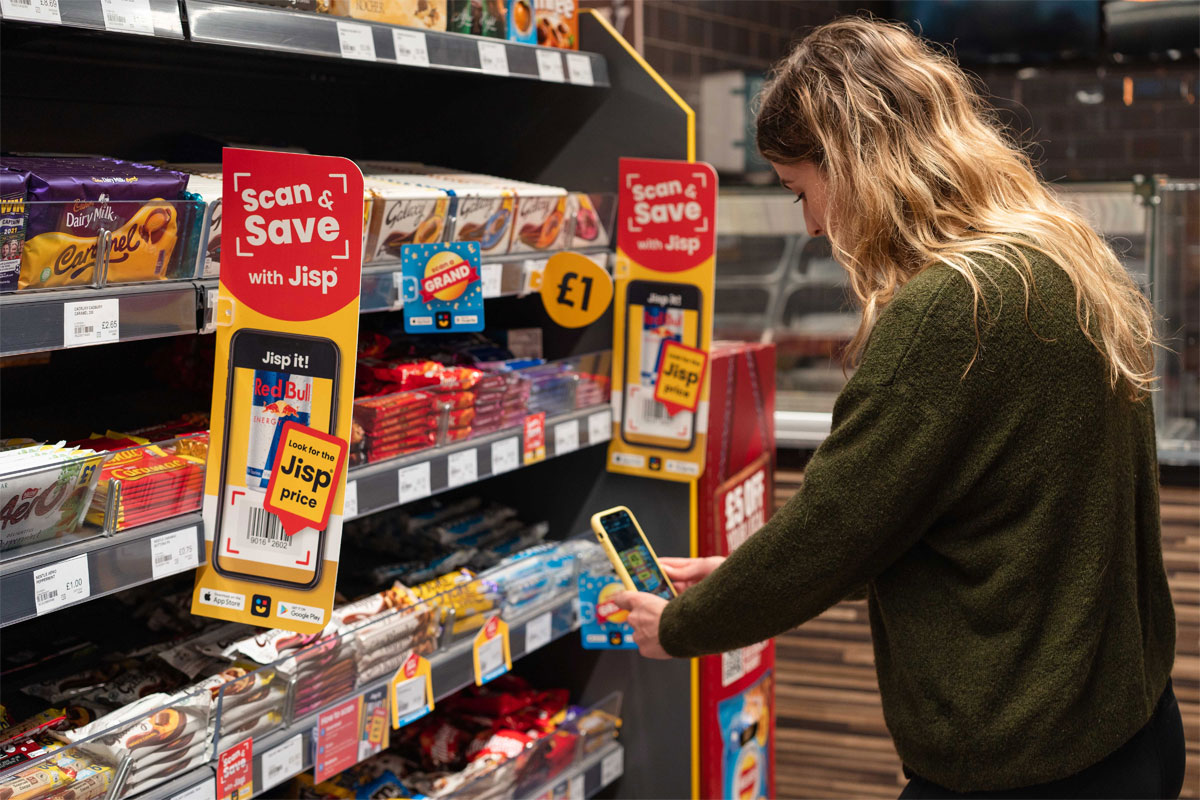 A woman uses her phone to redeem rewards of Jisp's Scan & Save app with promotions highlighting the app on store shelves.