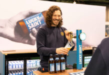 A person stands at a Lucky Saint branded beer tap pulling a pint with bottle of Lucky Saint in front of him.