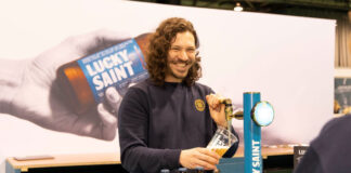 A person stands at a Lucky Saint branded beer tap pulling a pint with bottle of Lucky Saint in front of him.