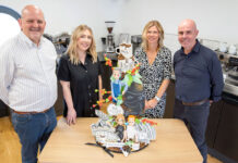 (left to right) Robert Milne, Rosluyn Coombe, Estelle MacGilp and Paul Chadderton all stand in a kitchen at a table with the 160th anniversary Matthew Algie cake.