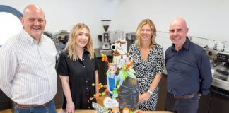 (left to right) Robert Milne, Rosluyn Coombe, Estelle MacGilp and Paul Chadderton all stand in a kitchen at a table with the 160th anniversary Matthew Algie cake.