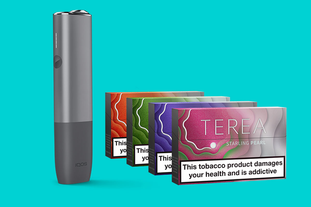 An IQOS ILUMA device with packs of Terea Pearls heat sticks against a teal blue background.