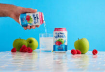 Lifestyle image of a person pouring a can of Radnor Splash into a glass with another can next to the glass and fruit around it.