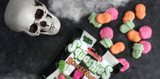 A packet of Swizzels Squashies Squeletons lie on a table with the sweets spilled out, above the packet is a skull and fog at the top and bottom of the image.