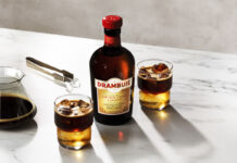 A bottle of Drambuie with two Drambuie Iced Espresso serves stand next to the bottle on a countertop.