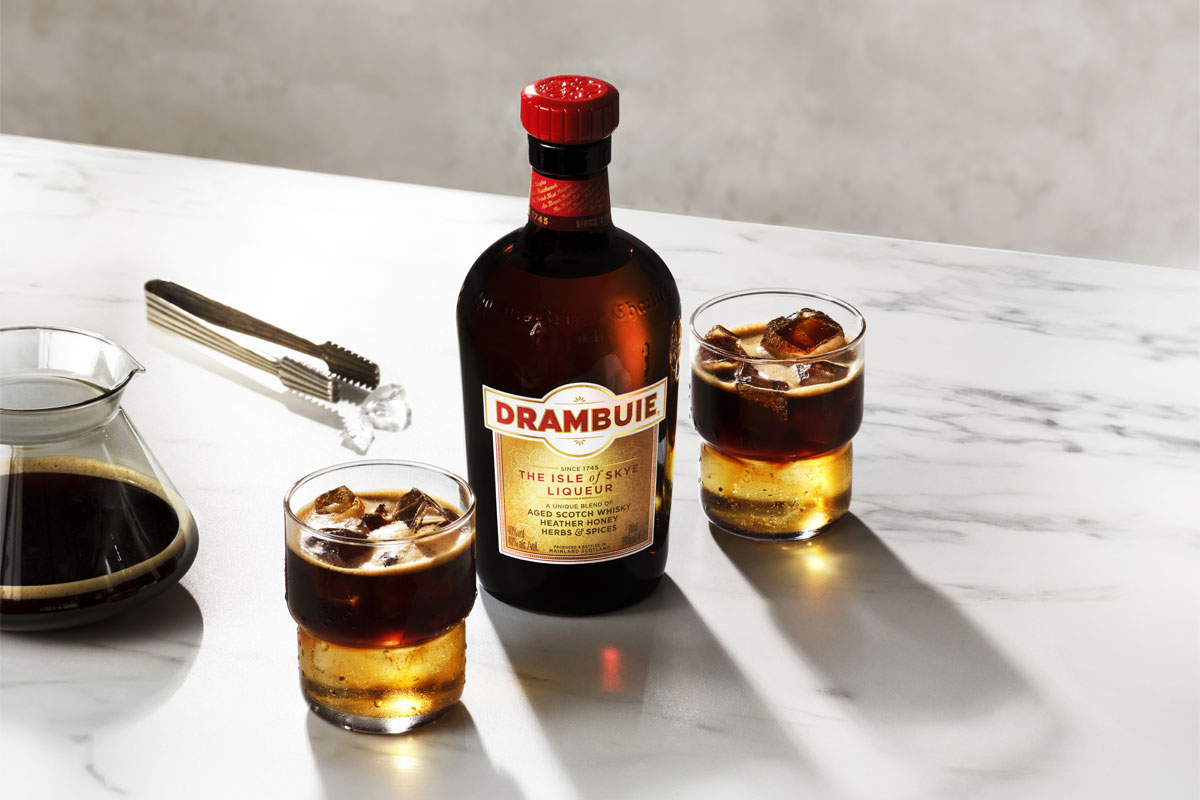 A bottle of Drambuie with two Drambuie Iced Espresso serves stand next to the bottle on a countertop.